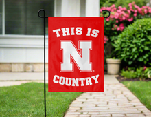 Load image into Gallery viewer, red university of nebraska country garden flag hanging in front of the yard