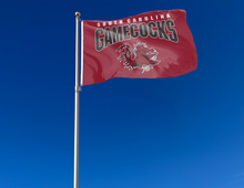 Load image into Gallery viewer, Red 3x5 University of South Carolina Gamecocks Flag with two metal grommets attached to flagpole waving in the wind