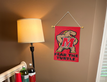 Load image into Gallery viewer, red university of maryland garden flag with fear the turtle logo hanging on banner pole inside living room