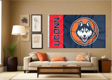 Load image into Gallery viewer, 3 by 5 foot UCONN Basketball Flag with two metal grommets covering the tan wall of a well-lit room