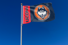 Load image into Gallery viewer, 3 by 5 foot UCONN Basketball Flag with two metal grommets attached to flagpole waving in the wind
