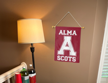 Load image into Gallery viewer, Maroon Alma College 13x18 Garden Flag with Alma A College Scots Logo hanging on a banner pole inside a well-lit room