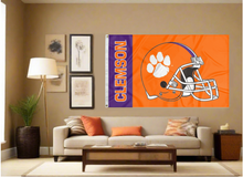 Load image into Gallery viewer, Orange and Purple striped 3x5 foot wide Clemson University Football Flag with two metal grommets covering the tan wall inside of a well organized room with couch pillows and light