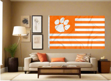 Load image into Gallery viewer, Clemson University Tigers National 3x5 foot wide flag with two metal grommets covering the tan wall inside of a well organized room with couch pillows and light