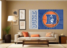Load image into Gallery viewer, Two Panel Blue and Gray Duke University 3x5 foot wide Flag with Duke Basketball Logo and two metal grommets covering the tan wall of the living room