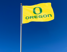 Load image into Gallery viewer, Gold University of Oregon Flag with O Oregon Logo attached to flagpole waving in the wind