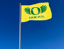 Load image into Gallery viewer, gold University of Oregon flag with Ducks logo attached to flagpole waving in the wind