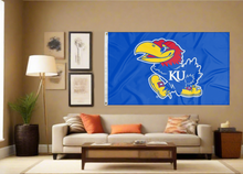 Load image into Gallery viewer, Blue 3x5 foot wide University of Kansas Flag with Jayhawks logo and two metal grommets covering tan wall of a well-lit room