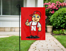 Load image into Gallery viewer, lil red nebraska mascot garden flag hung outside from a garden flag stand