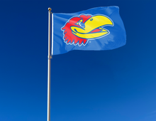 Load image into Gallery viewer, University of Kansas flag with Jayhawk head logo hung on a flagpole for tailgate decor