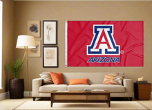 Load image into Gallery viewer, Red 3x5 foot wide University of Arizona Flag with two metal grommets for indoor home decor covering the tan wall of well-lit room