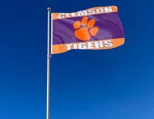 Load image into Gallery viewer, 3x5 feet wide Clemson University Flag with orange purple and orange stripes and two metal grommets attached to flagpole waving in the wind