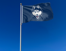 Load image into Gallery viewer, Navy 3x5 foot wide University of Connecticut (UCONN) Huskies flag with husky head logo and two metal grommets attached to flagpole waving in the wind