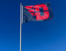 Load image into Gallery viewer, Dark blue 3x5 foot wide University of Dayton Flying D Flag with red D logo and two metal grommets attached to flagpole waving in the wind