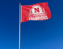 Load image into Gallery viewer, Red 3x5 feet wide University of Nebraska Huskers BIG Ten Conference Volleyball 2024 Champions Flag with two metal grommets attached to flagpole waving in the wind