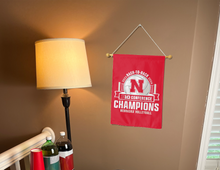 Load image into Gallery viewer, Red 13x18 inches long University of Nebraska Huskers BIG Ten Conference Volleyball 2024 Champions Garden Flag hanging on black garden flag stand hanging on banner pole covering tan wall of a well-lit room