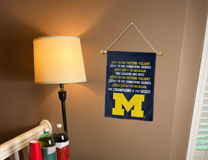blue michigan wolverines fight song garden flag hung on a banner pole next to a lamp and drinks