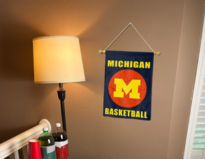 blue michigan basketball logo garden flag hung on a banner pole next to a lamp and drinks