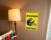 Load image into Gallery viewer, Gold Michigan Football logo garden flag hung on a banner pole next to a lamp.
