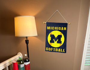 blue Michigan Softball garden flag hung from a banner pole next to a lamp and drinks.