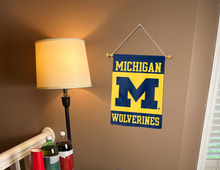 Load image into Gallery viewer, blue and gold Michigan wolverines garden flag hung from banner pole inside living room
