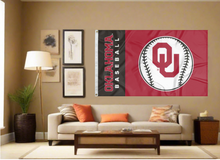 Load image into Gallery viewer, black and red University of Oklahoma baseball flag with two metal grommets covering tan wall of well lit room
