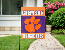 Load image into Gallery viewer, three panel orange and purple clemson garden flag hung outside from garden flag stand 
