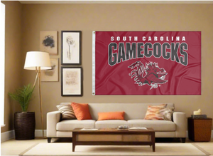 Red 3x5 University of South Carolina Gamecocks Flag with two metal grommets covering tan wall of well lit room