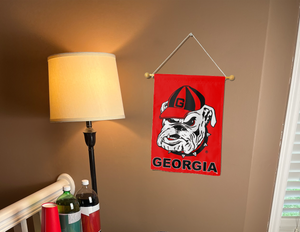 Red Georgia Bulldogs garden flag hanging on a beige wall next to a lamp.