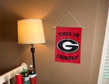 Load image into Gallery viewer, georgia garden flag with this is country logo hanging on banner pole next to lamp and drinks indoors
