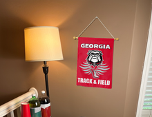 Load image into Gallery viewer, red georgia track and field garden flag hanging on banner pole next to a lamp drinks, and cups
