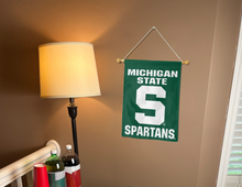Load image into Gallery viewer, green michigan state university garden flag with S spartans logo hanging on banner pole inside living room
