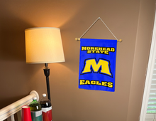 Load image into Gallery viewer, blue morehead state garden flag with M eagles logo hanging on a banner pole inside a living room

