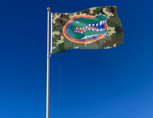 Load image into Gallery viewer, 3x5 foot-wide University of Florida Flag with Camo Background and two metal grommets attached to flagpole waving in the wind
