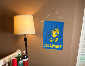 blue University of Delaware YoUDee Garden Flag hung from banner pole inside living room