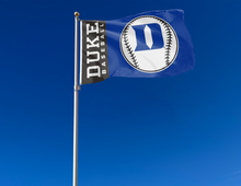 Load image into Gallery viewer, Blue and Black 3x5 Duke Baseball Flag with two metal grommets attached to flagpole waving in the wind
