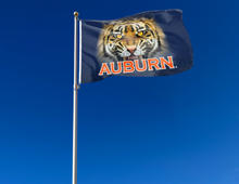 Load image into Gallery viewer, blue 3x5 foot wide Auburn University flag with Realistic Tiger face over Auburn logo and two metal grommets attached to flagpole waving in the wind
