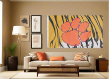 Load image into Gallery viewer, 3x5 foot wide Clemson University Flag with Tiger Skin and Stripes Background and two metal grommets covering the tan wall inside of a well organized room with couch pillows and light
