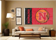 Load image into Gallery viewer, Black and Red 3x5 Nebraska Basketball Flag covering the tan wall of a well lit room under a couch
