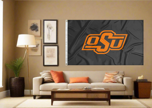 Black 3x5 feet wide Oklahoma State University Flag with OSU Logo and two metal grommets for indoor home decor covering tan wall of well lit room