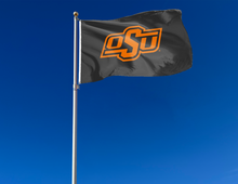 Load image into Gallery viewer, Black 3x5 feet wide Oklahoma State University Flag with OSU Logo and two metal grommets for outdoor home decor attached to flagpole waving in the wind
