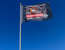 Load image into Gallery viewer, Navy blue 3x5 foot wide UCONN flag with big east men&#39;s basketball tournament 2024 champions uconn huskies logo and two metal grommets attached to flagpole waving in the wind
