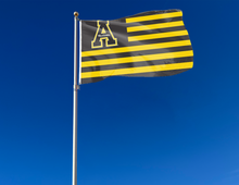 Load image into Gallery viewer, Black and Gold stripes 3x5 foot wide Appalachian State University flag with two metal grommets attached to flagpole waving in the wind

