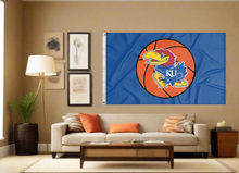 Load image into Gallery viewer, 3x5 University of Kansas Basketball Flag with two metal grommets for indoor home decor covering the tan wall of a well-lit room
