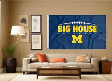 Load image into Gallery viewer, Blue 3x5 foot wide University of Michigan Flag with Big House Football M Logo and two metal grommets covering the tan wall of a well-lit room
