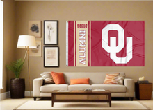 Load image into Gallery viewer, Red 3x5 feet wide University of Oklahoma Alumni Flag with two metal grommets for indoor home decor covering the tan wall of a well-lit room
