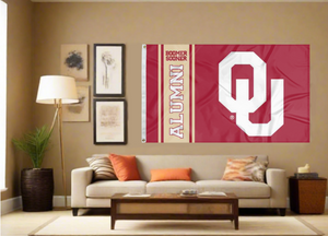 Red 3x5 feet wide University of Oklahoma Alumni Flag with two metal grommets for indoor home decor covering the tan wall of a well-lit room