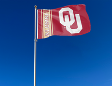 Load image into Gallery viewer, Red 3x5 feet wide University of Oklahoma Alumni Flag with two metal grommets for outdoor home decor attached to flagpole waving in the wind

