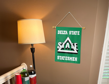 Load image into Gallery viewer, green delta state university garden flag hung from banner pole inside living room
