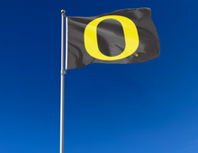 Load image into Gallery viewer, Black University of Oregon flag attached to flagpole waving in the wind
